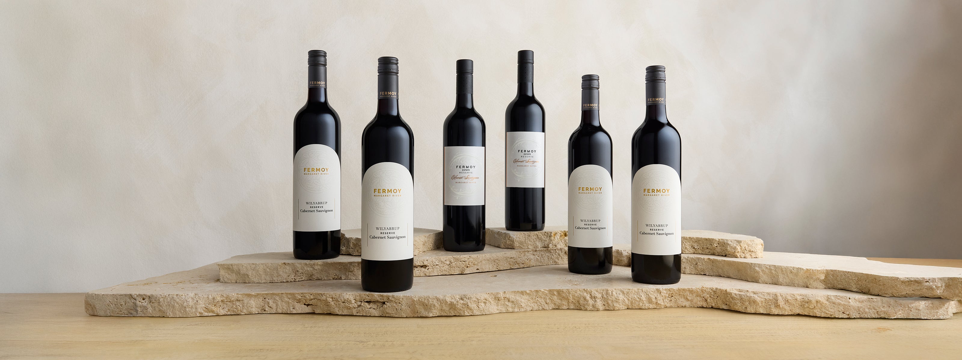 Row of wine bottles on a stone tray with a neutral background